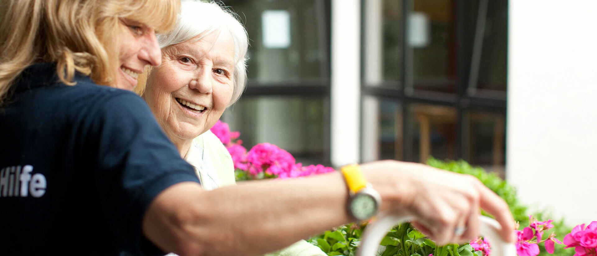 Bewohnerin und Pflegekraft gießen Blumen. Szene aus dem betreuten Wohnen. 